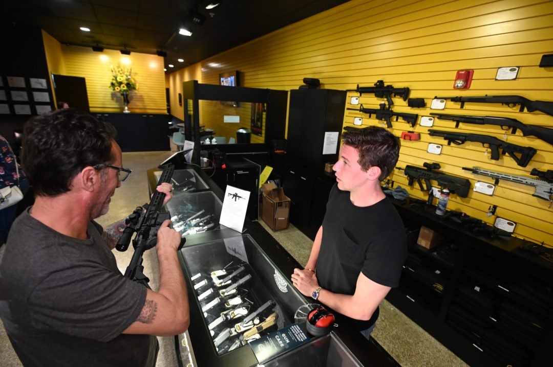 Customer examines a rifle at a gun store counter