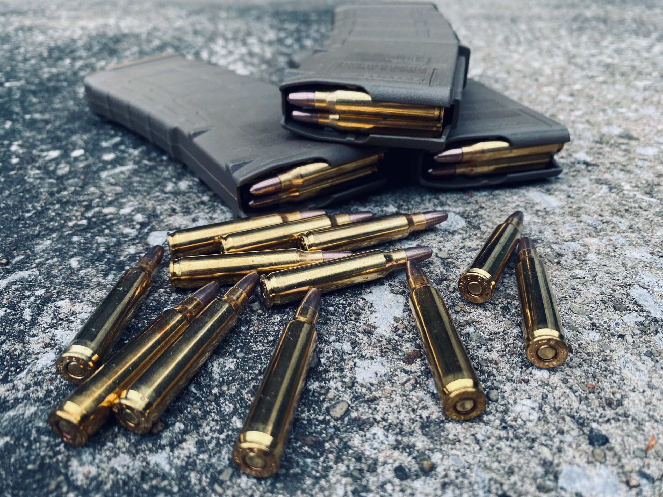 Lead-free frangible rifle ammunition with brass casings displayed beside three black rifle magazines on a concrete surface.