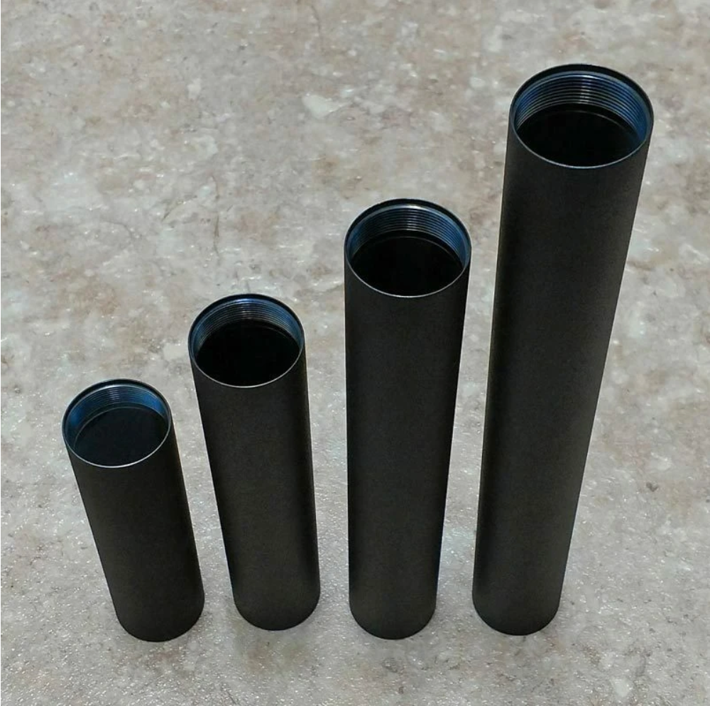 Four black cylindrical solvent trap tubes of varying lengths with threaded openings displayed on a gray stone surface.